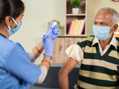 Doctor preparing vaccination shot to elderly patient by holding syringe at home - concept of home health check to seniors during coronavirus covid-19 pandemic