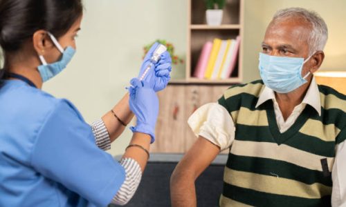 Doctor preparing vaccination shot to elderly patient by holding syringe at home - concept of home health check to seniors during coronavirus covid-19 pandemic